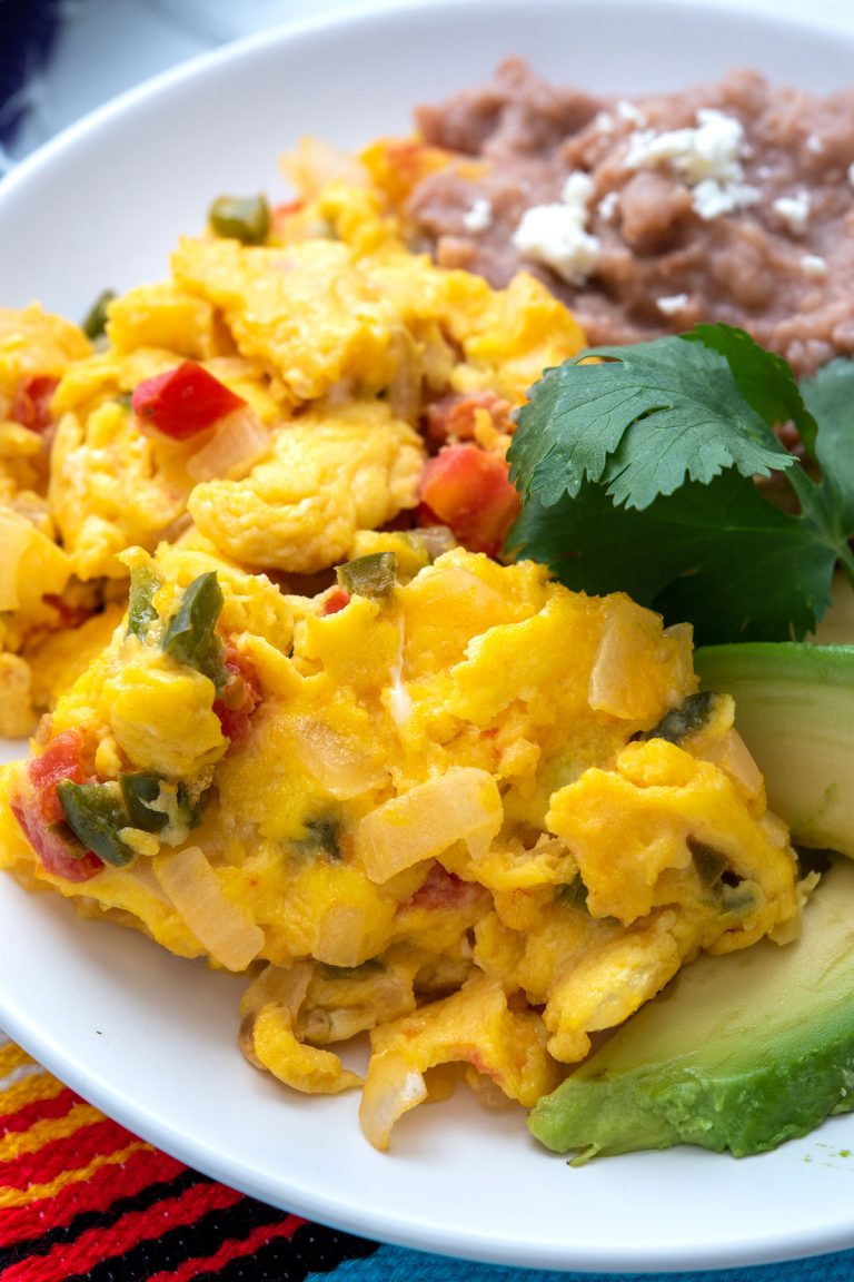 Plate of huevos a la mexicana with avocado and refried beans on the side