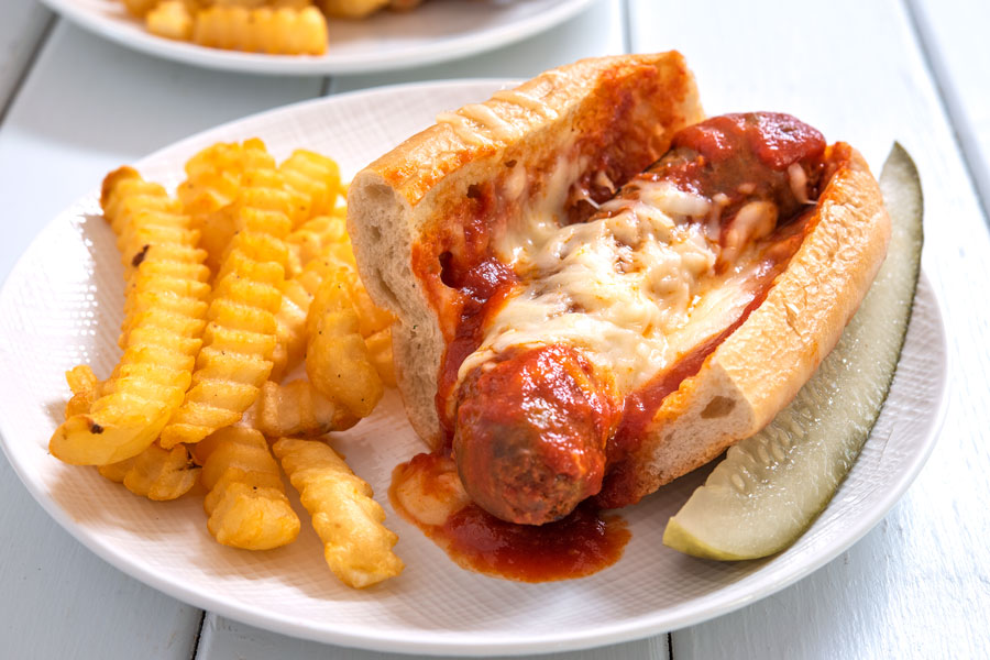 Plate of Italian sausage sandwich with a side of fries and pickle