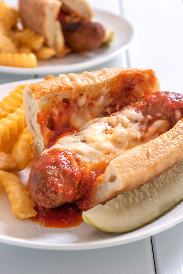 Plate of Italian sausage sandwich with a side of fries and pickle