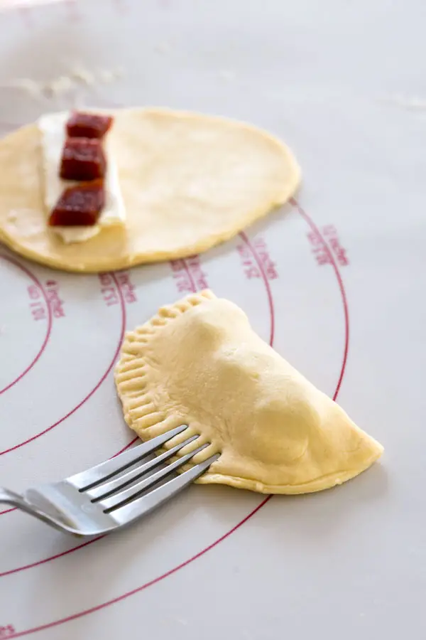 Uncooked guava empanadas with cream cheese being sealed with a fork