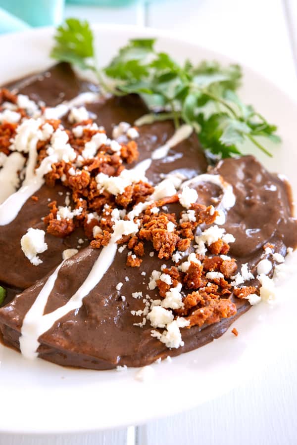 4 black bean enfrijoladas on a plate sprinkled with chorizo, queso and crema