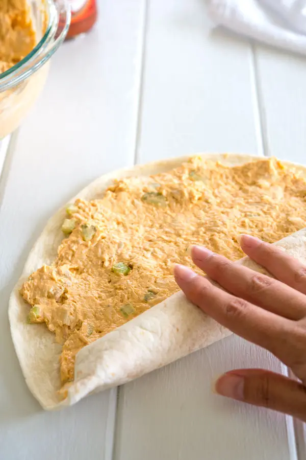 Buffalo chicken filling (cream cheese, chicken, hot sauce) being rolled up in tortillas