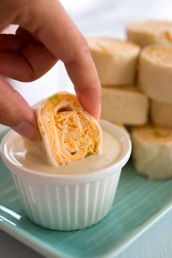 One buffalo chicken roll up being dipped in small bowl of ranch