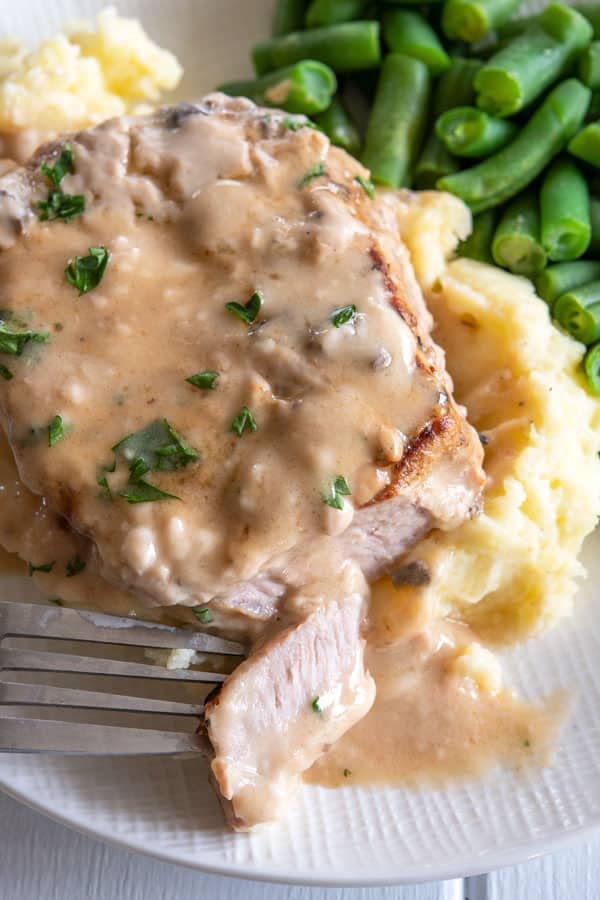 Baked pork chop on mashed potatoes with a piece sliced onto a fork and ready to eat