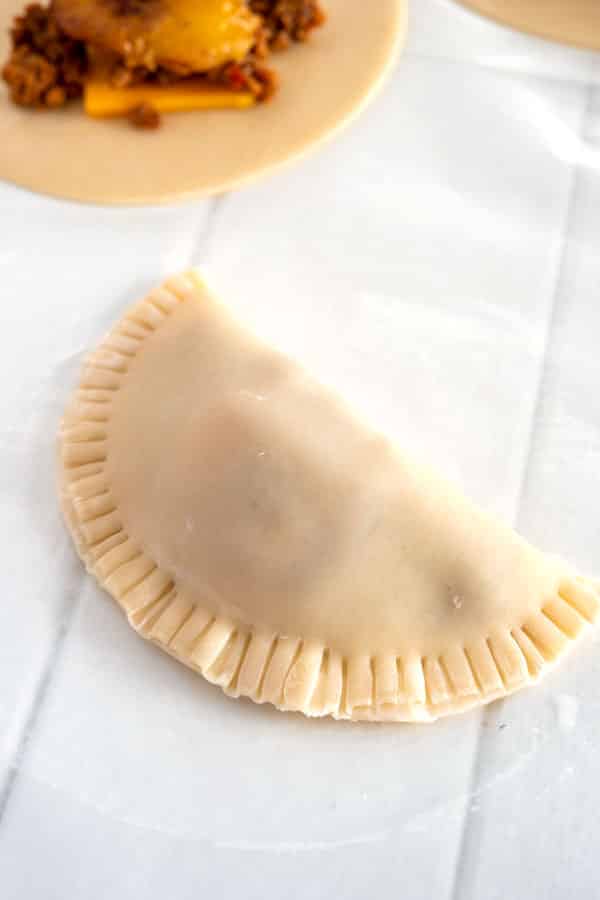 Uncooked empanada folded in half with crimped edges