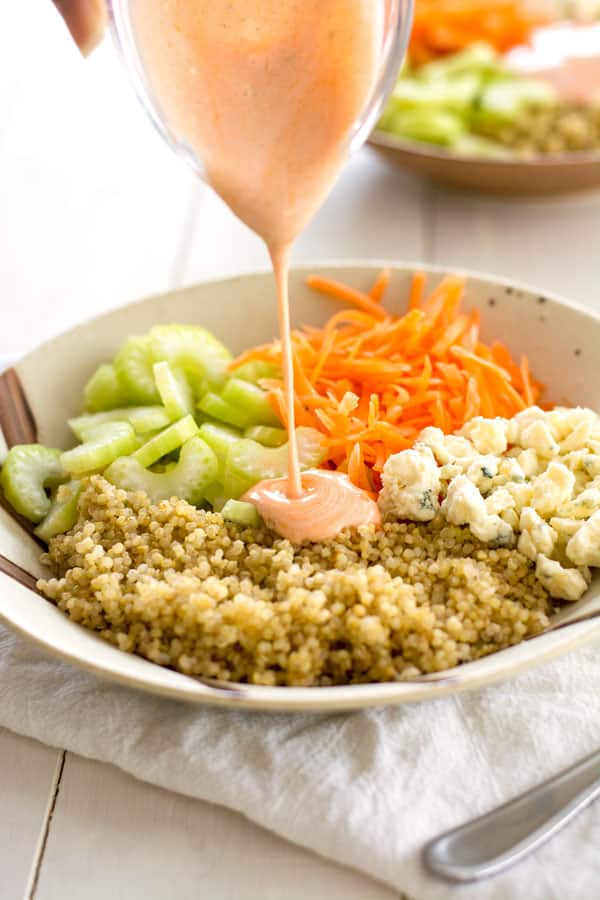 Buffalo Chicken Quinoa Bowl with blue cheese, celery and carrots being drizzled with creamy hot sauce dressing