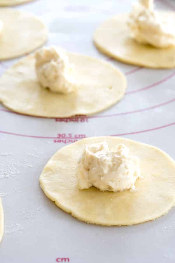 Making sopapilla cheesecake hand pies: Mini rounds of pie crust with a tablespoon of cream cheese filling in center