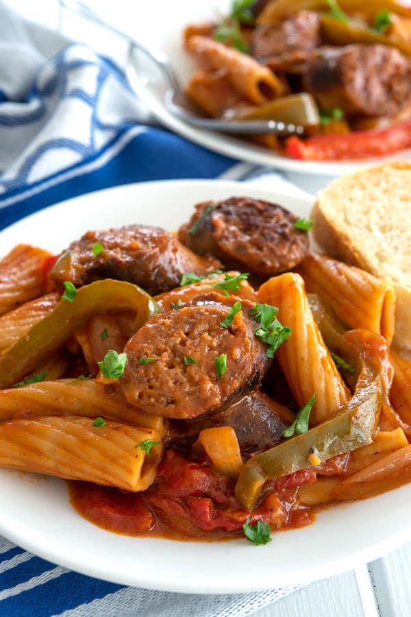 Sausage and peppers pasta on a plate with a side of Italian bread