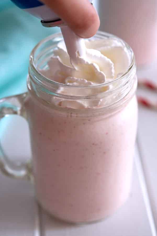 Glass of strawberry milkshake without ice cream being topped with whipped cream