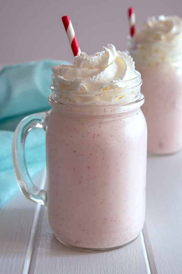 Mason jar glass full of strawberry milkshake without ice cream and whipped cream on top