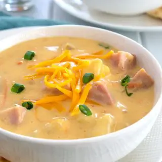 Bowl of cheesy ham and potato soup with cheddar, potatoes and green onions