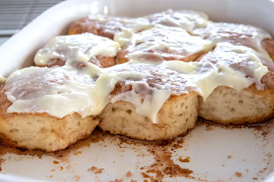 Half empty baking dish of cinnamon biscuits with cream cheese frosting