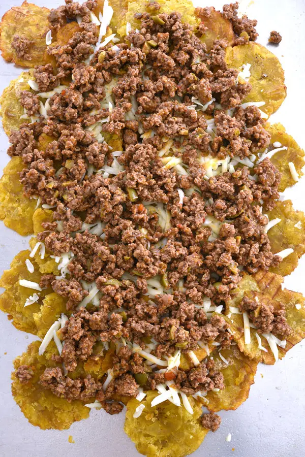Layers of tostones, cheese and picadillo on cookie sheet for tostone nachos