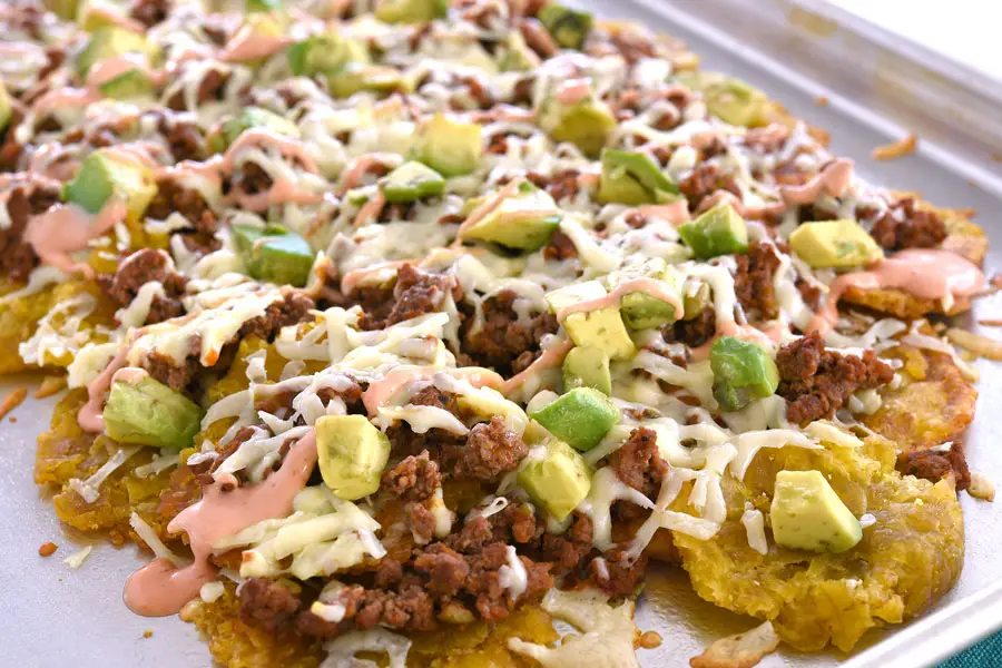 Pan of tostone nachos layered with ground beef, cheese, avocado and mayoketchup