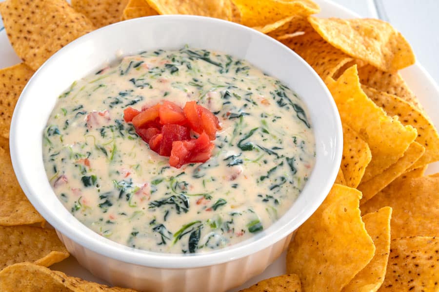 Small bowl of spinach cheese dip surrounded by tortilla chips