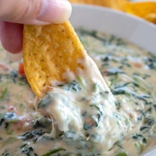 Tortilla chip being dunked into spinach cheese dip