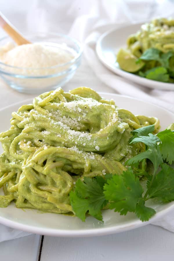 White plate with espagueti verde garnished with grated cheese and cilantro
