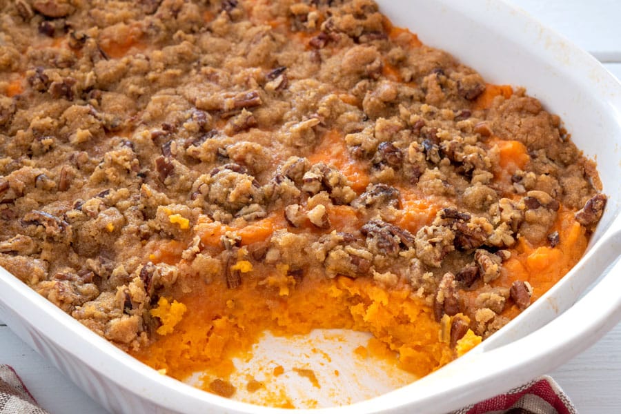 White casserole dish of sweet potato casserole with pecans and brown sugar topping