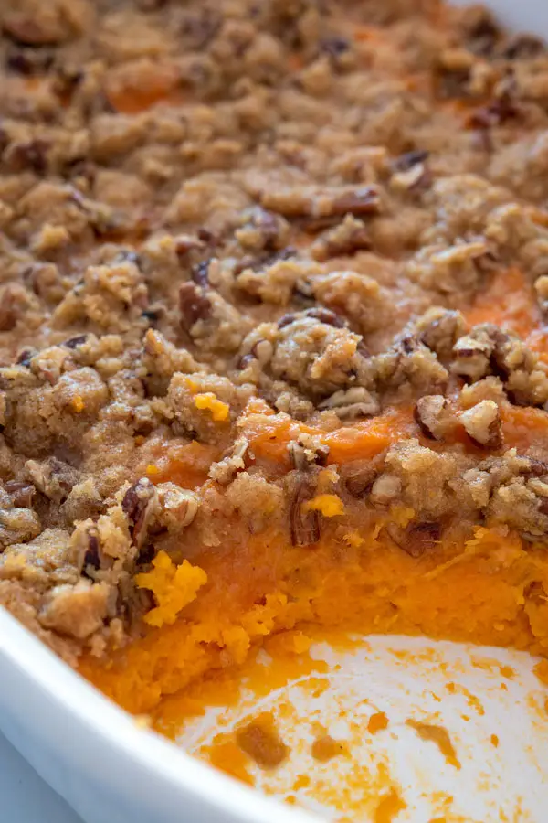 White casserole dish of sweet potato casserole with pecans and brown sugar topping