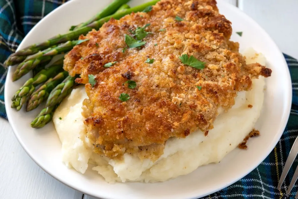 breaded chicken breast over mashed potatoes with asparagus