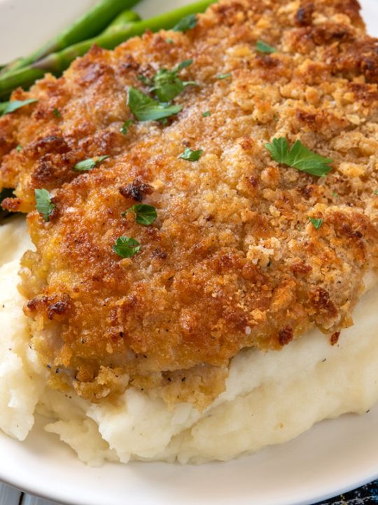 breaded chicken breast over mashed potatoes with asparagus